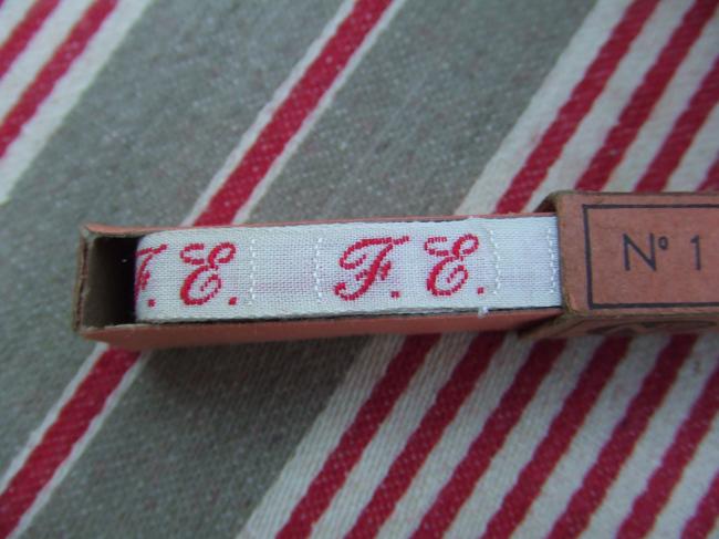 Boite de ruban blanc avec initiales 'FE' tissées en rouge 1920, Household Gem